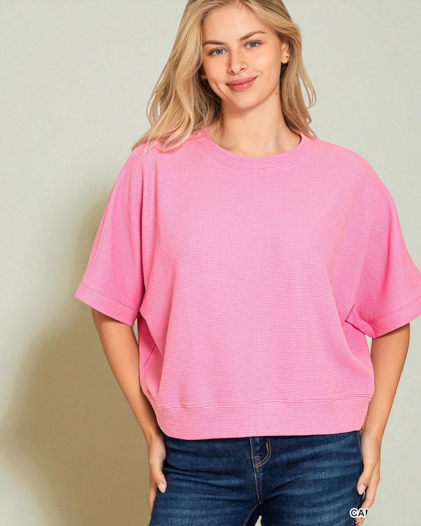 Woman wearing a pink oversized shirt and blue jeans against a beige background