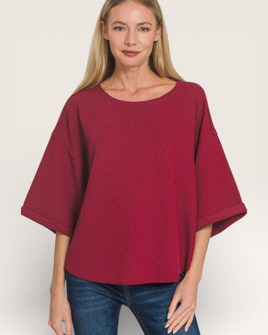 Woman wearing a burgundy poncho over a blue top on a white background