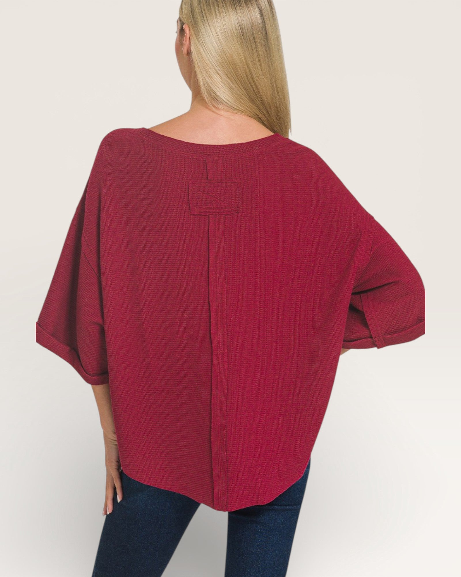 Person wearing a burgundy poncho on a plain background
