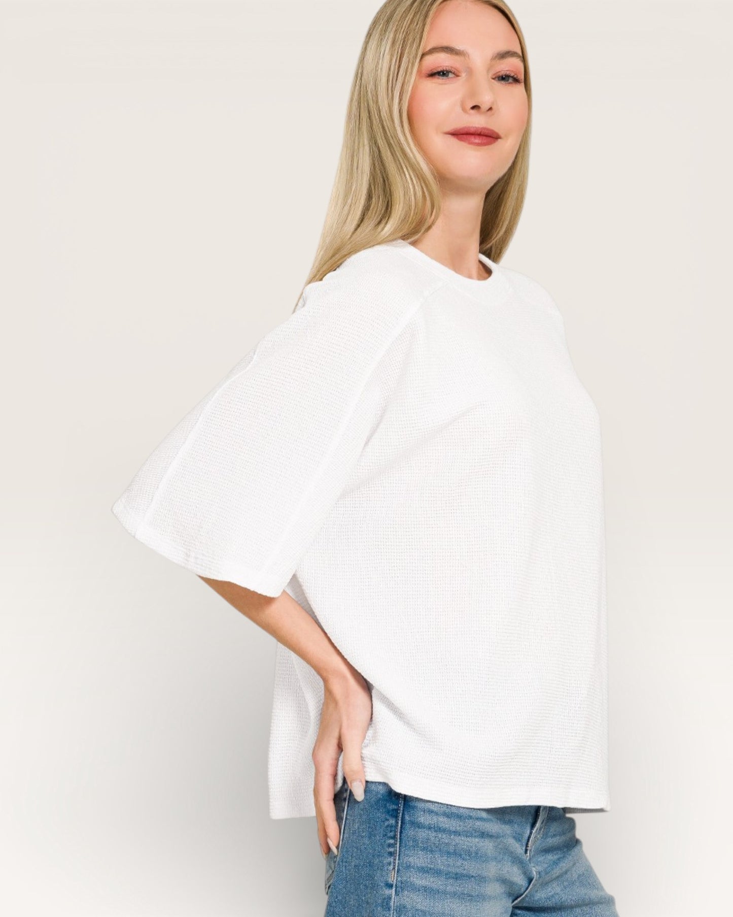 Woman wearing a white oversized t-shirt and blue jeans against a plain background