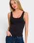 A woman wearing a black scoop-neck tank top and blue jeans, photographed against a plain light gray studio background.