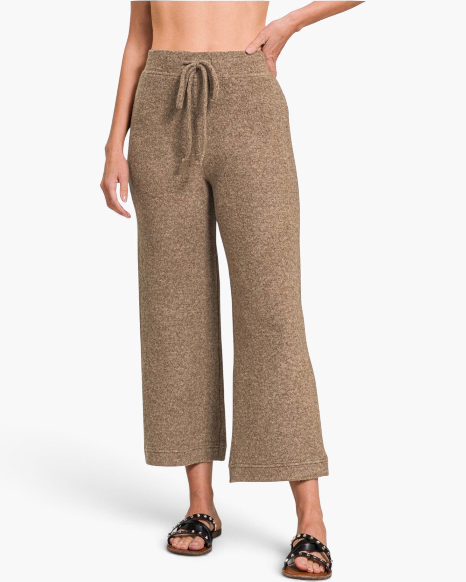 A model wearing a pair of wide-leg cropped pants in a heathered taupe-brown color, paired with black slide sandals, against a clean white studio background.