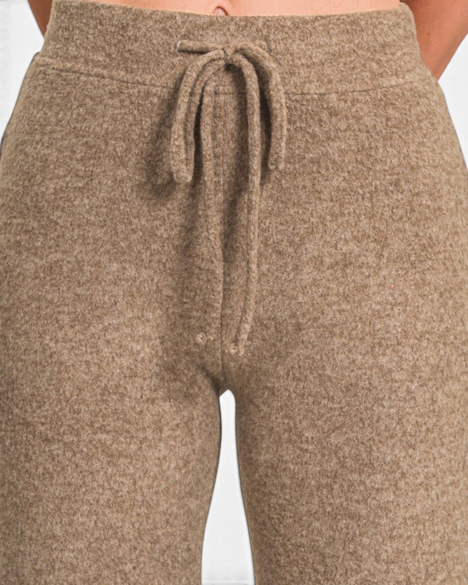Close-up of a person wearing heathered taupe-brown knit pants with a drawstring waistband, shown against a plain light background.