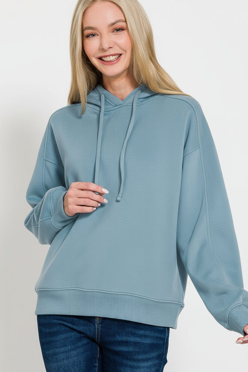 Woman wearing a light blue hoodie against a solid blue background