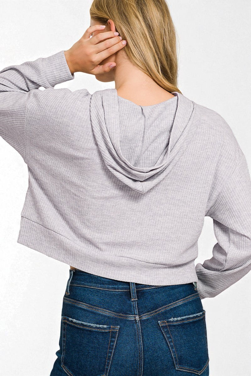 Person wearing a light gray ribbed hoodie and blue jeans on a white background