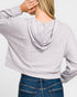 Person wearing a light gray ribbed hoodie and blue jeans on a plain background