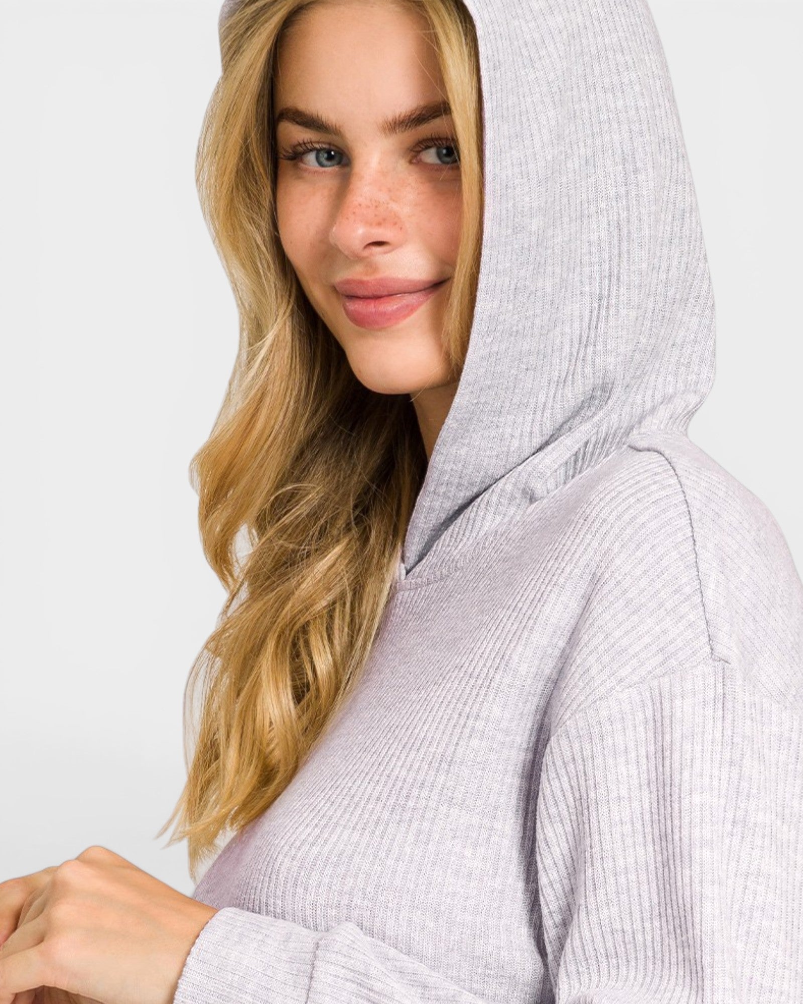 Woman wearing a light gray hooded outfit against a plain background