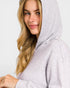 Woman wearing a light gray hooded outfit against a plain background