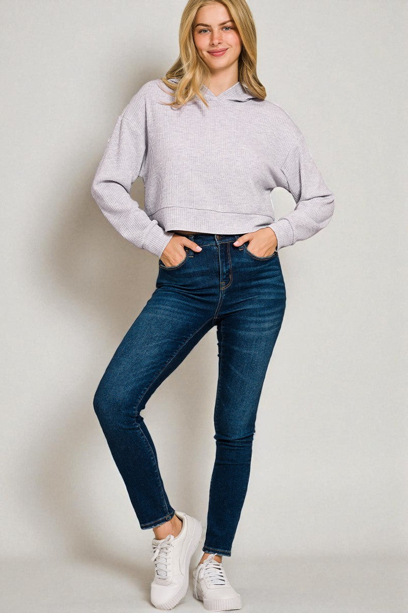 Woman wearing a gray hoodie and blue jeans against a plain background