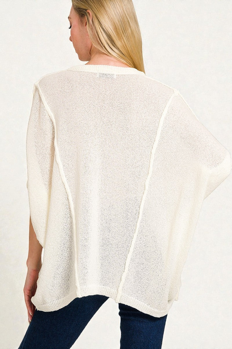 Woman wearing a white poncho over a blue outfit on a plain background