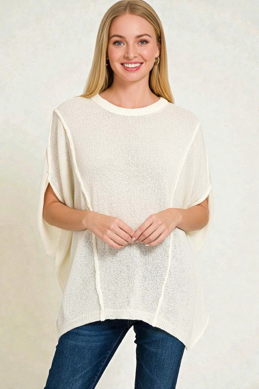 Woman wearing a white poncho over a blue top on a plain background