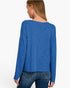 A woman shown from the back wearing a blue long-sleeve knit top and dark blue jeans against a plain white studio background.