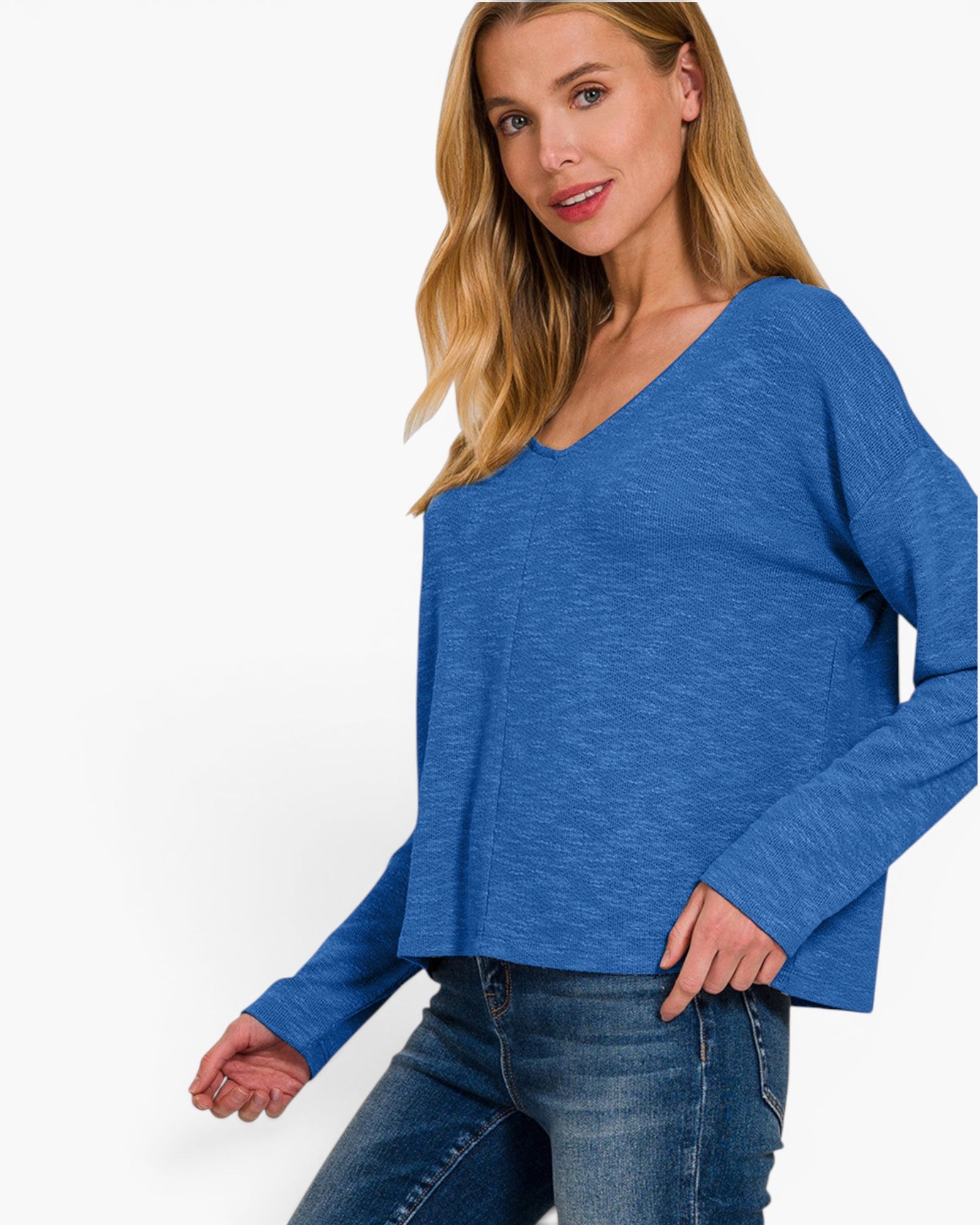 A woman wearing a heathered blue long-sleeve V-neck top and blue jeans, photographed against a clean white studio background.