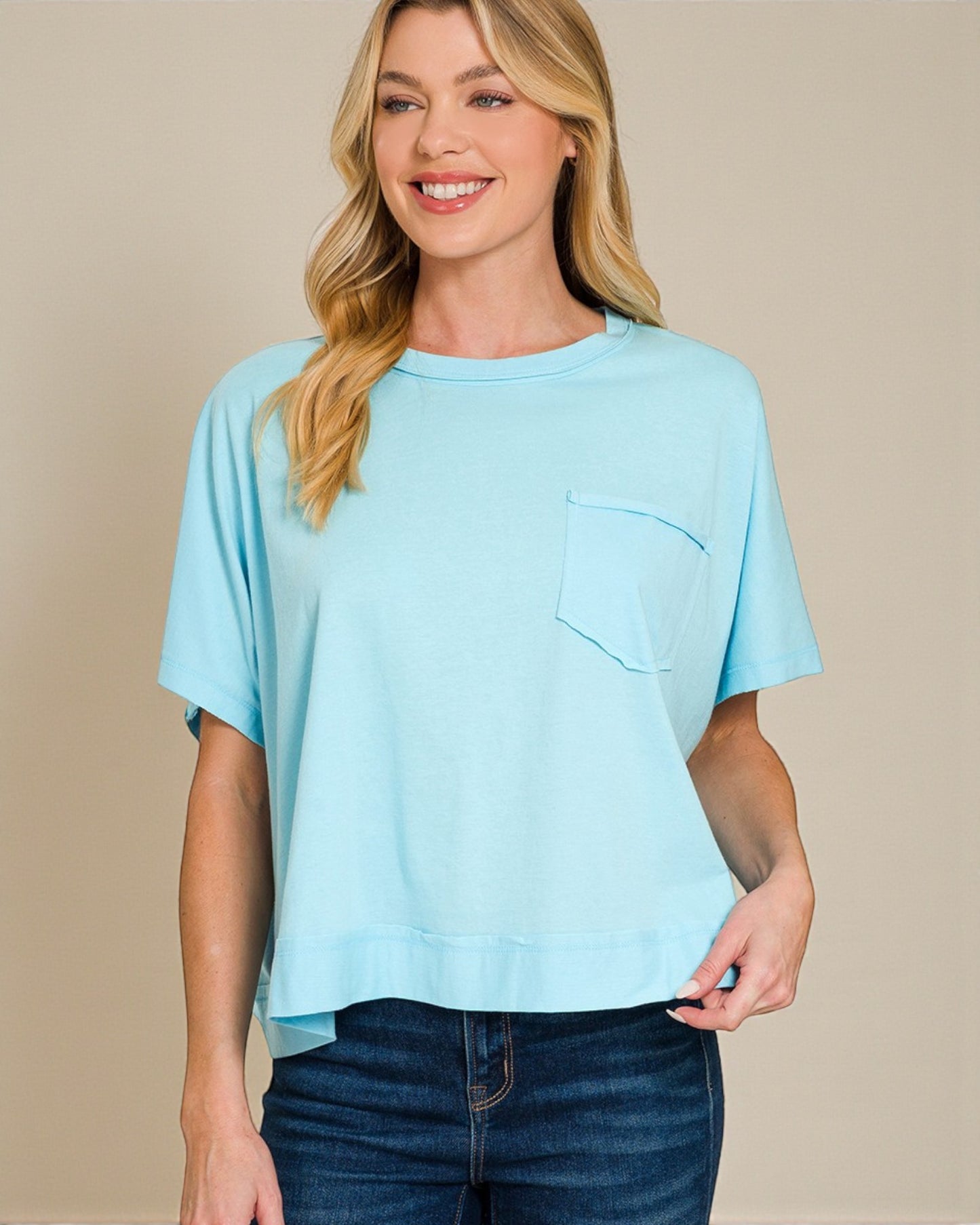 Woman wearing a light blue t-shirt with a pocket on a beige background