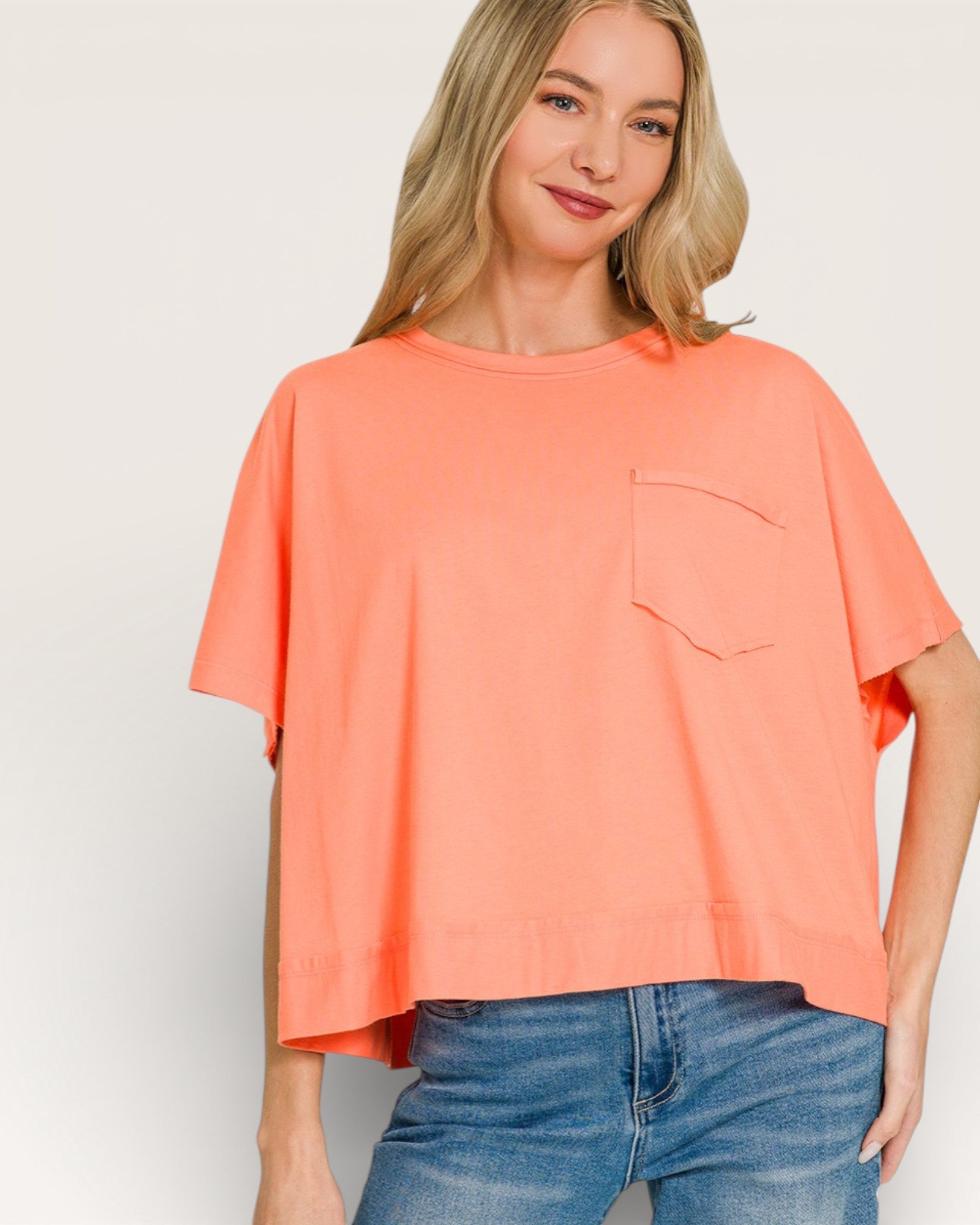 Woman wearing a coral oversized t-shirt with a pocket on a plain background