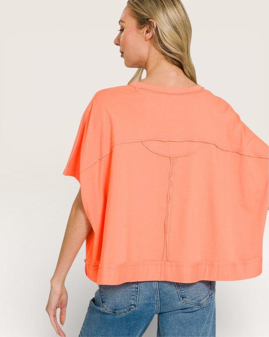 Woman wearing a coral oversized top and blue jeans on a white background