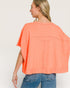 Woman wearing a coral oversized top and blue jeans on a white background