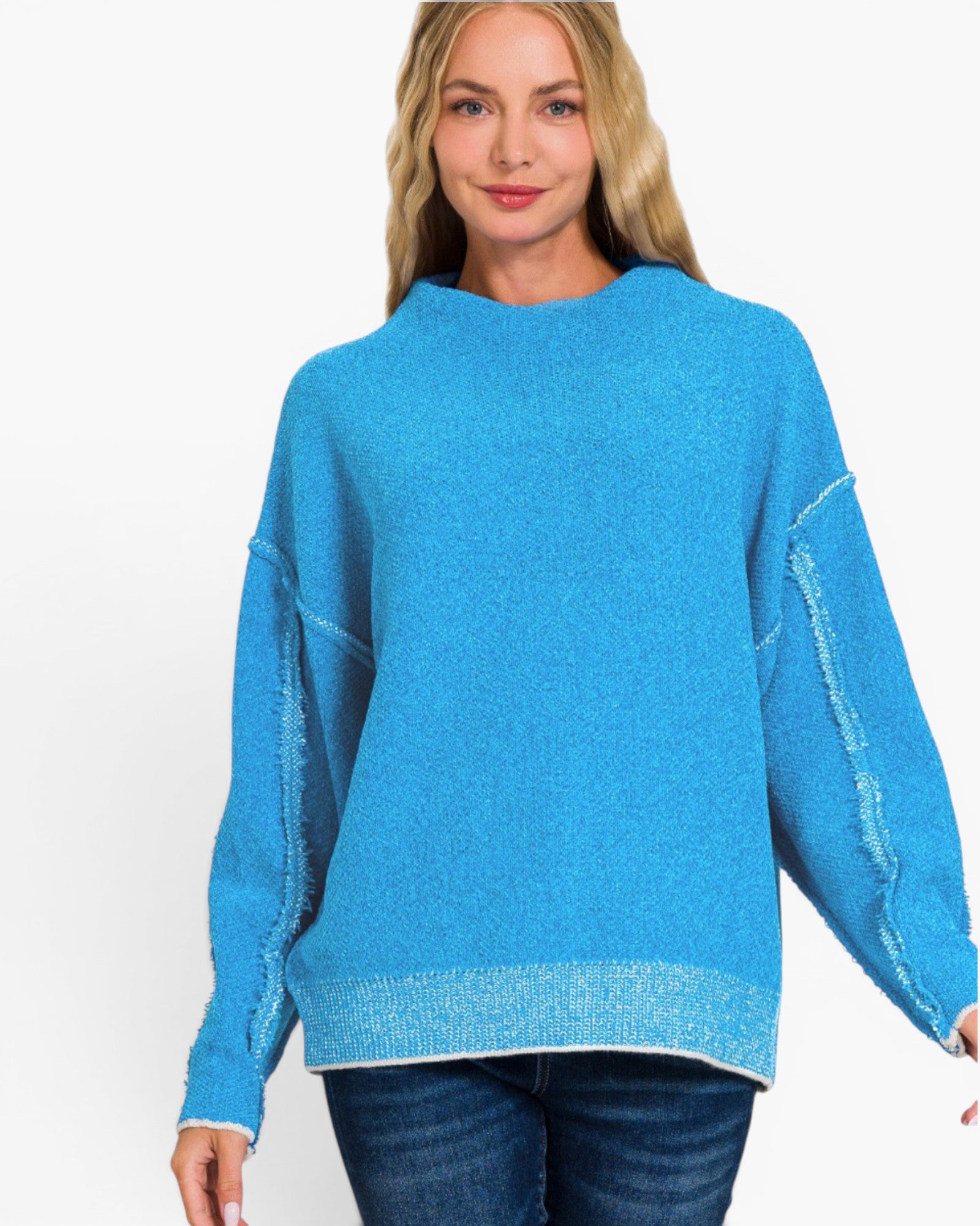 A woman wearing a bright turquoise blue knit sweater with textured, frayed sleeve details and a ribbed hem, paired with dark blue jeans, against a plain white background.