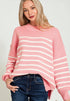 Woman wearing a pink and white striped sweater with blue jeans on a plain background