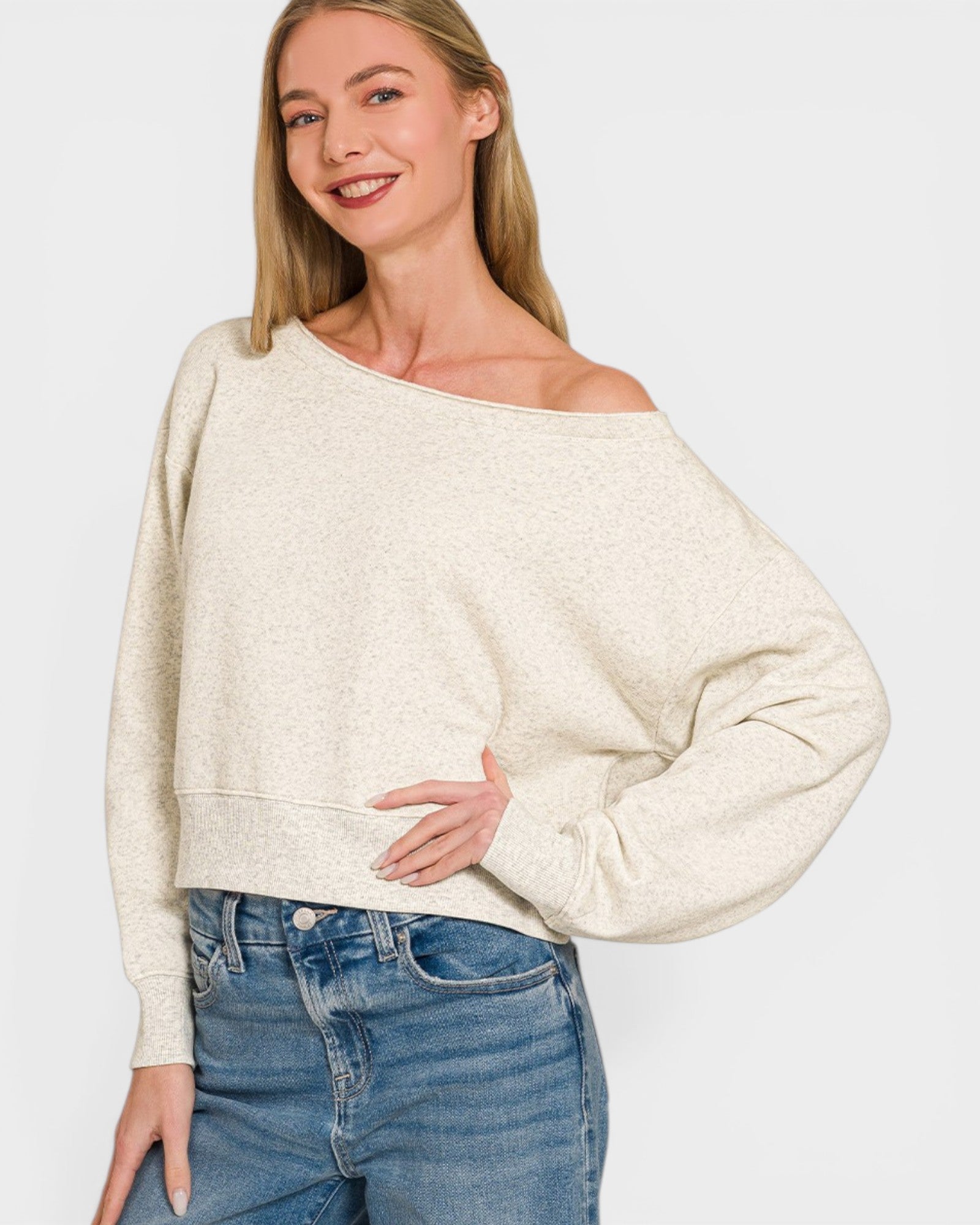 Woman wearing a beige off-shoulder sweater and blue jeans on a white background