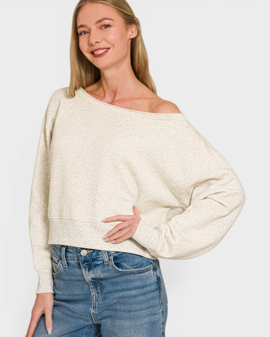 Woman wearing a beige off-shoulder sweater and blue jeans on a white background