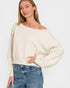 Woman wearing a beige off-shoulder sweater and blue jeans on a white background