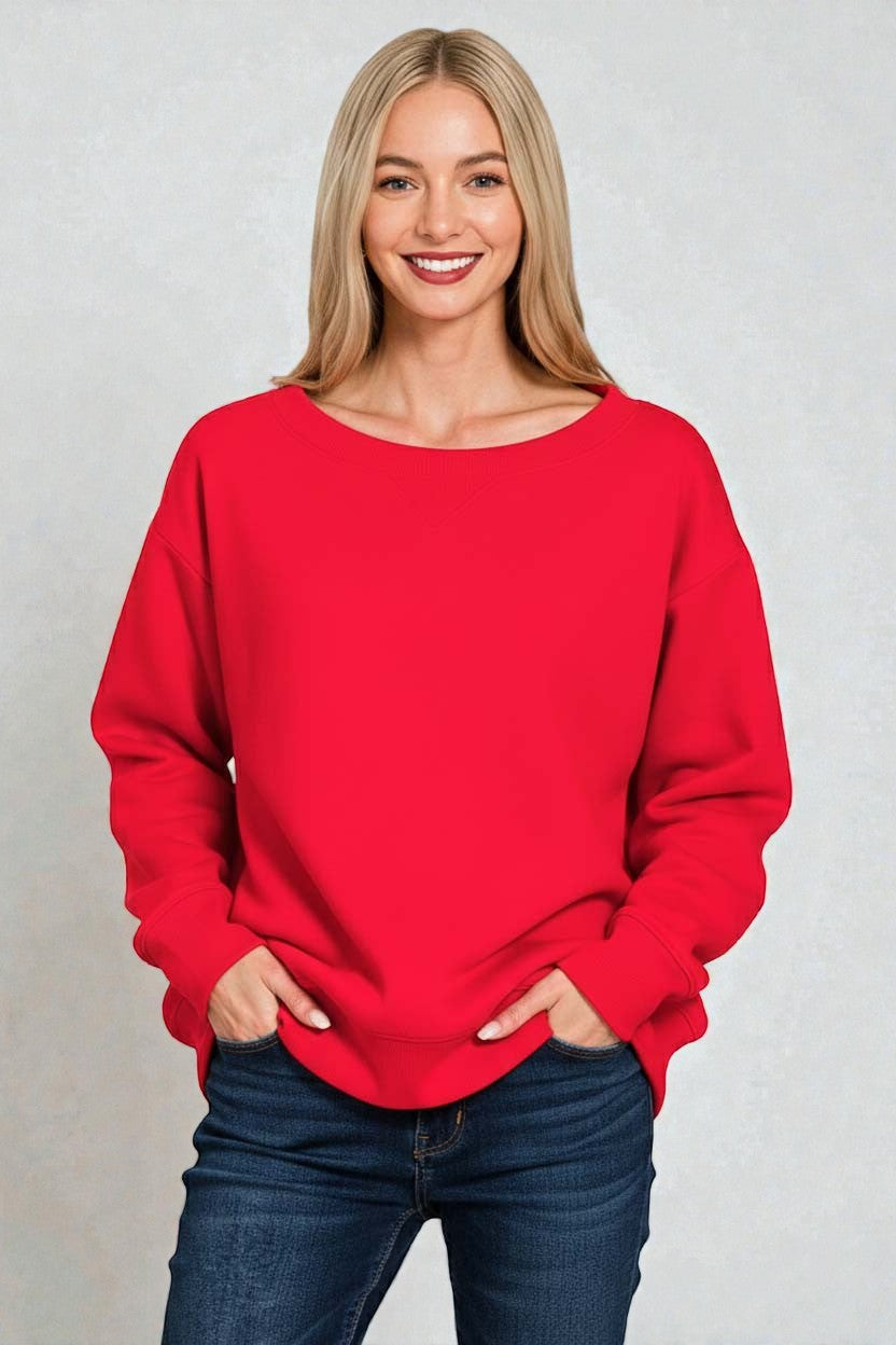 Woman wearing a red sweater and blue jeans against a plain background