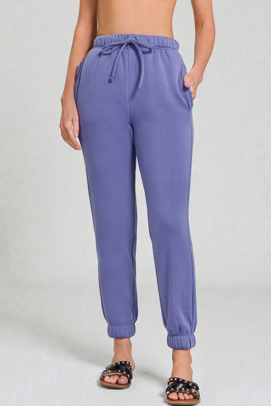 Purple sweatpants worn by a person on a plain background