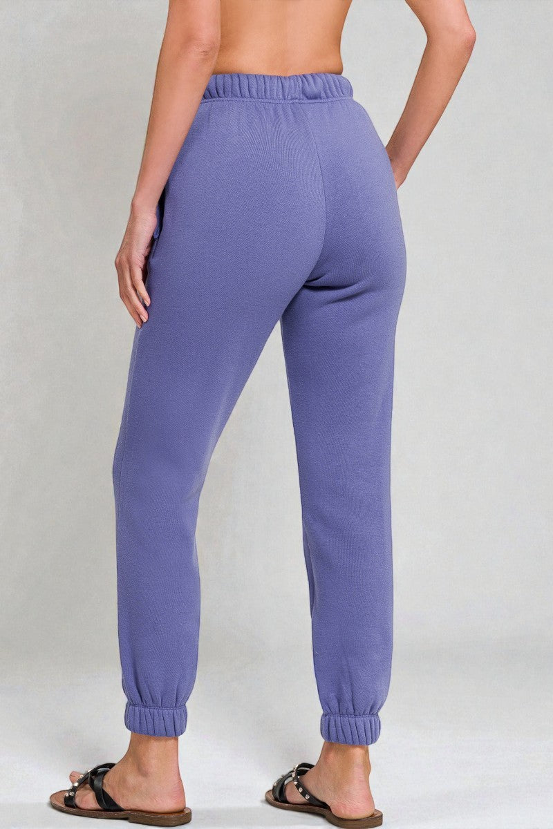 Purple sweatpants worn by a person on a plain background