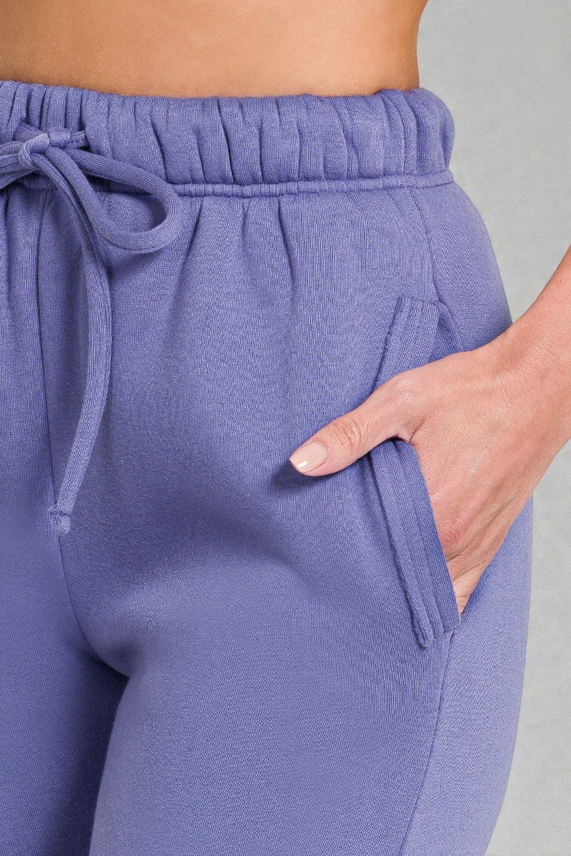 Purple sweatpants with a drawstring waist and pocket on a gray background