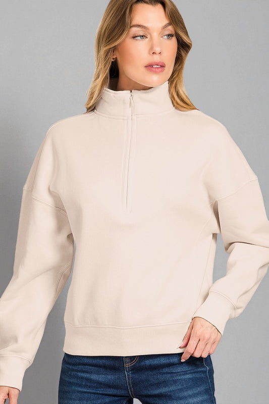 Woman wearing a beige half-zip sweatshirt against a gray background