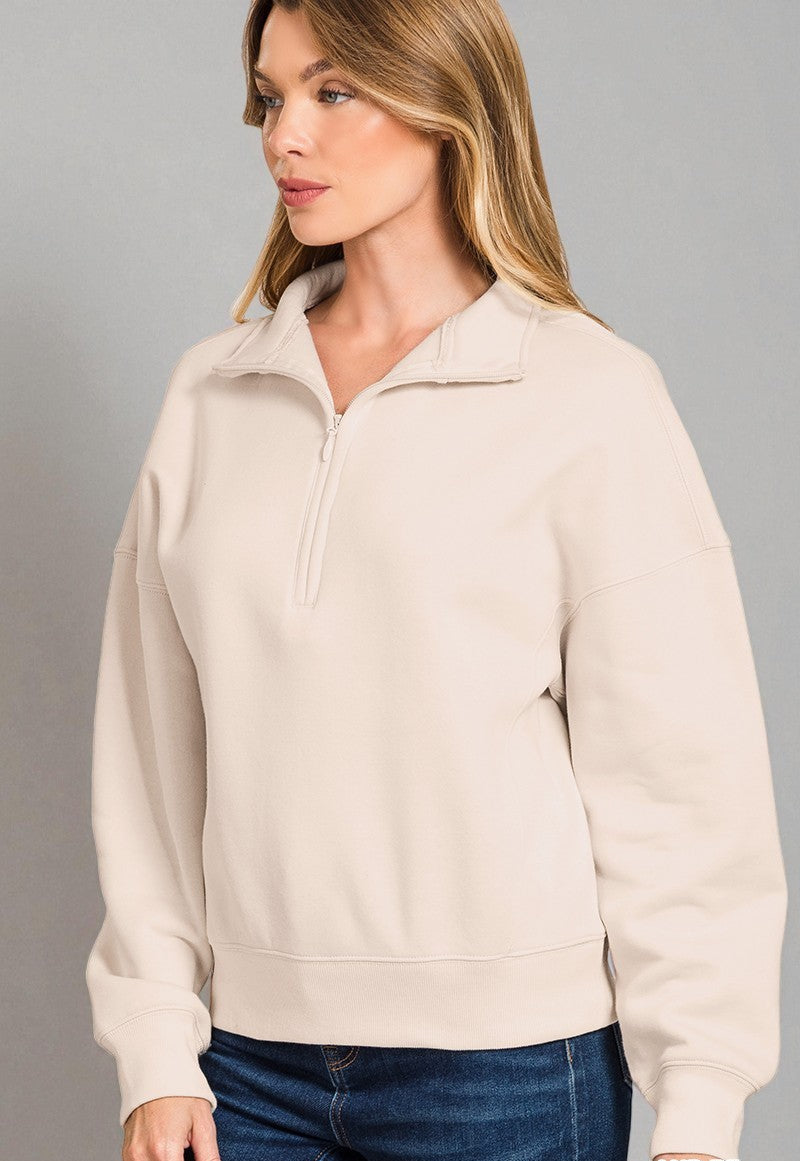 Woman wearing a beige pullover with a zipper on a gray background