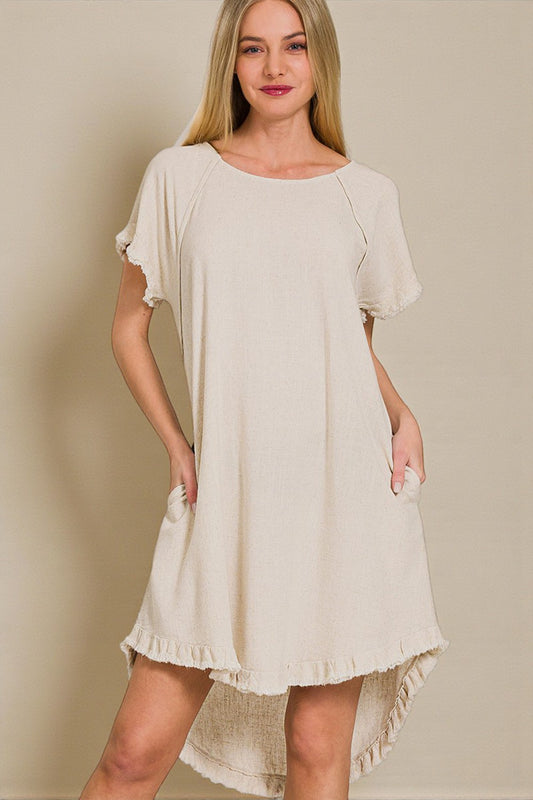 Woman wearing a beige dress with ruffled sleeves and hem against a plain background