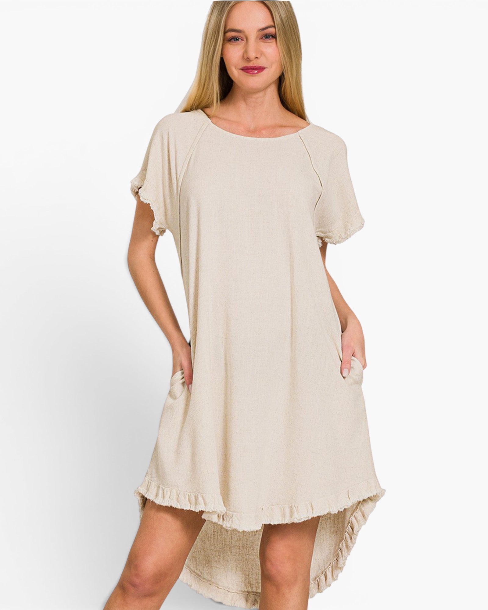 A woman modeling a light beige short-sleeve high-low dress with ruffled trim and side pockets, set against a plain white studio background.