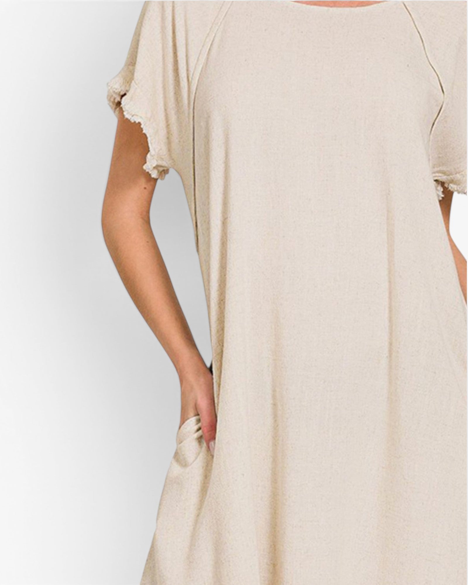 A close-up of a person wearing a loose, short-sleeve beige dress or tunic with ruffled sleeve edges and side pockets, shown against a plain light background.