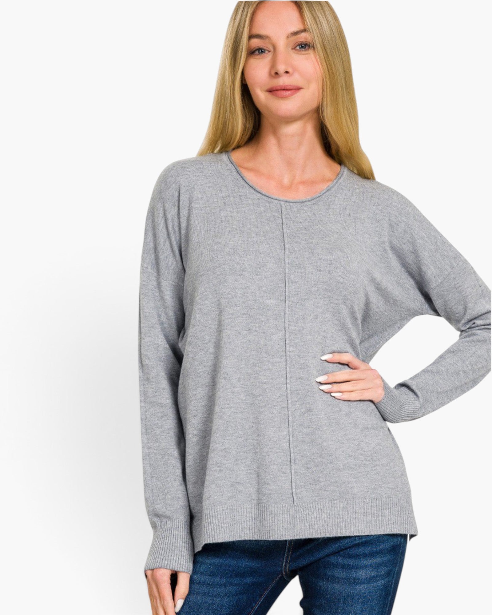 A woman wearing a light gray long-sleeve knit sweater with a relaxed, slightly oversized fit and a subtle vertical seam detail at the center front, paired with blue jeans against a plain white background.