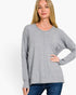 A woman wearing a light gray long-sleeve knit sweater with a relaxed, slightly oversized fit and a subtle vertical seam detail at the center front, paired with blue jeans against a plain white background.