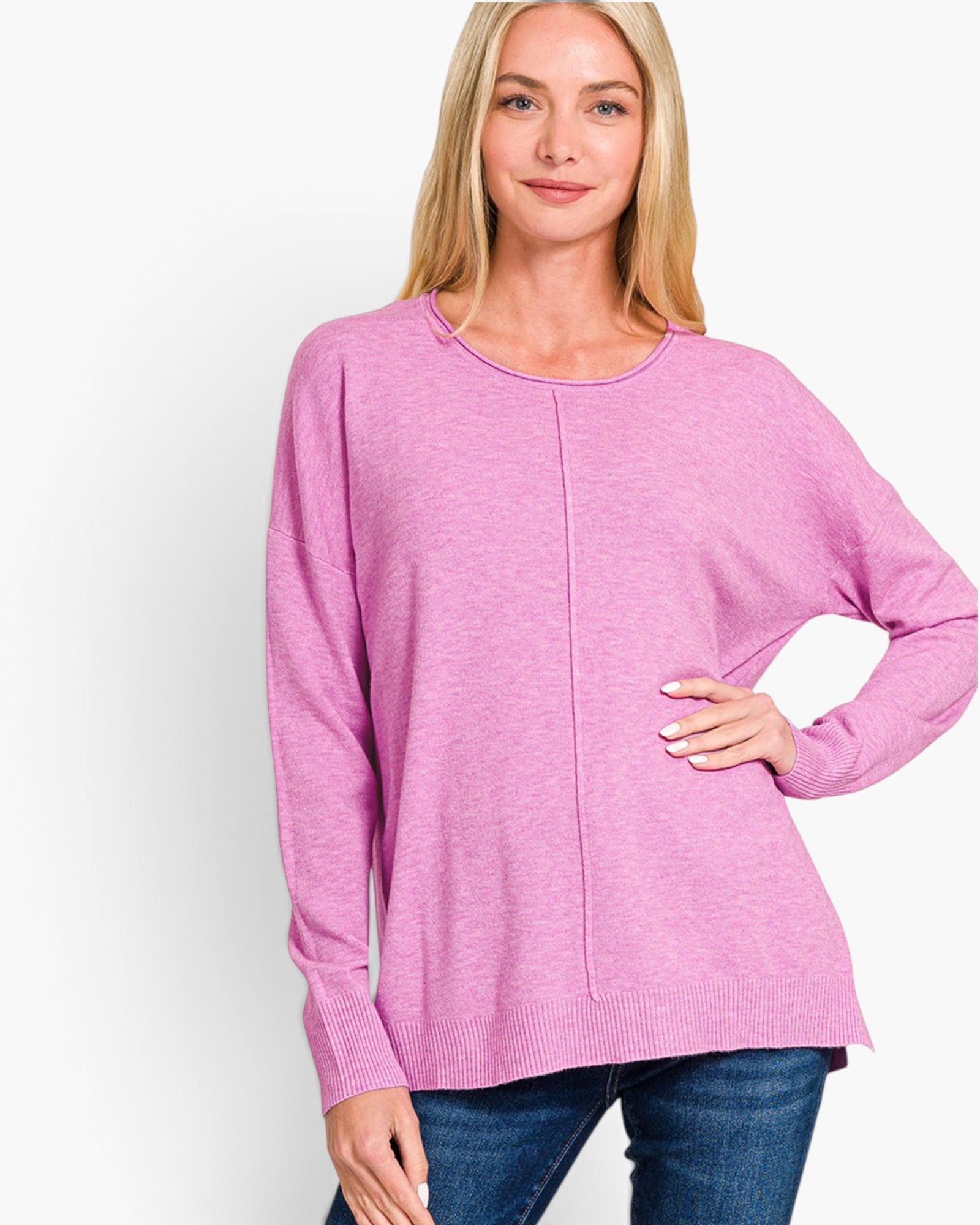 A woman wearing a pink long-sleeve knit sweater with a crew neck and a central seam detail, paired with blue jeans, against a plain white background.