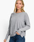 A woman wearing a light gray knit sweater with a boat neckline and long sleeves, paired with blue jeans, photographed against a clean white studio background.