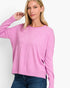 A woman wearing a pink long-sleeve knit sweater with a crew neck and front seam detail, paired with blue jeans, against a plain white studio background.