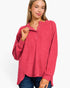 A woman wearing a heathered pink long-sleeve henley top with a buttoned collar, paired with blue jeans, against a plain white background.