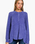 A woman wearing a heathered periwinkle blue long-sleeve henley top with a buttoned neckline, paired with dark blue jeans, against a plain white background.