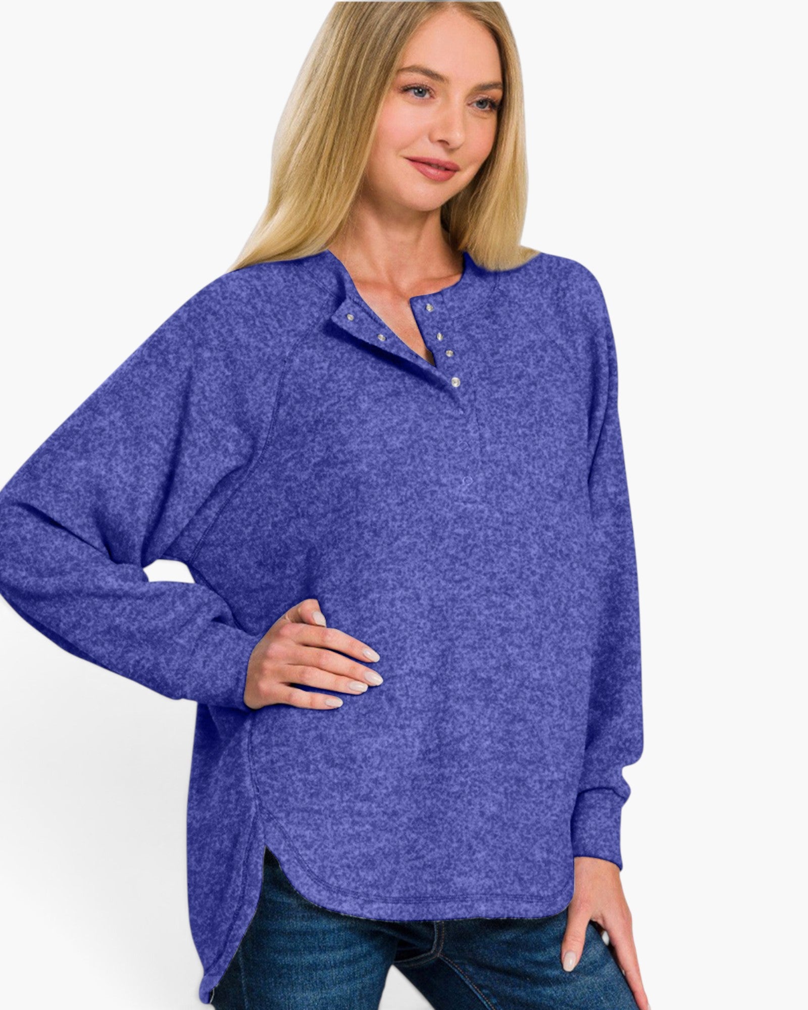 A woman wearing a heathered periwinkle blue long-sleeve henley top with a buttoned collar, paired with dark blue jeans, against a plain white background.