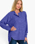 A woman wearing a heathered periwinkle blue long-sleeve henley top with a buttoned collar, paired with dark blue jeans, against a plain white background.