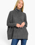 A woman wearing a dark gray heathered turtleneck sweater with long sleeves and a relaxed fit, paired with blue jeans, against a plain white background.