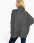 A woman shown from the back wearing a dark gray heathered knit poncho sweater with a high folded collar and wide draped sleeves, paired with blue jeans, against a plain white studio background.
