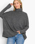 A woman wearing a dark gray heathered knit turtleneck sweater with long sleeves and a relaxed fit, paired with blue jeans, against a plain white background.