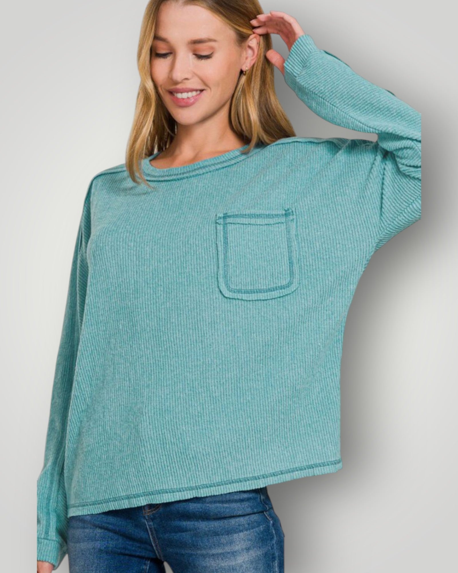 Woman wearing a teal sweater with a pocket against a plain background