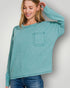 Woman wearing a teal sweater with a pocket against a plain background