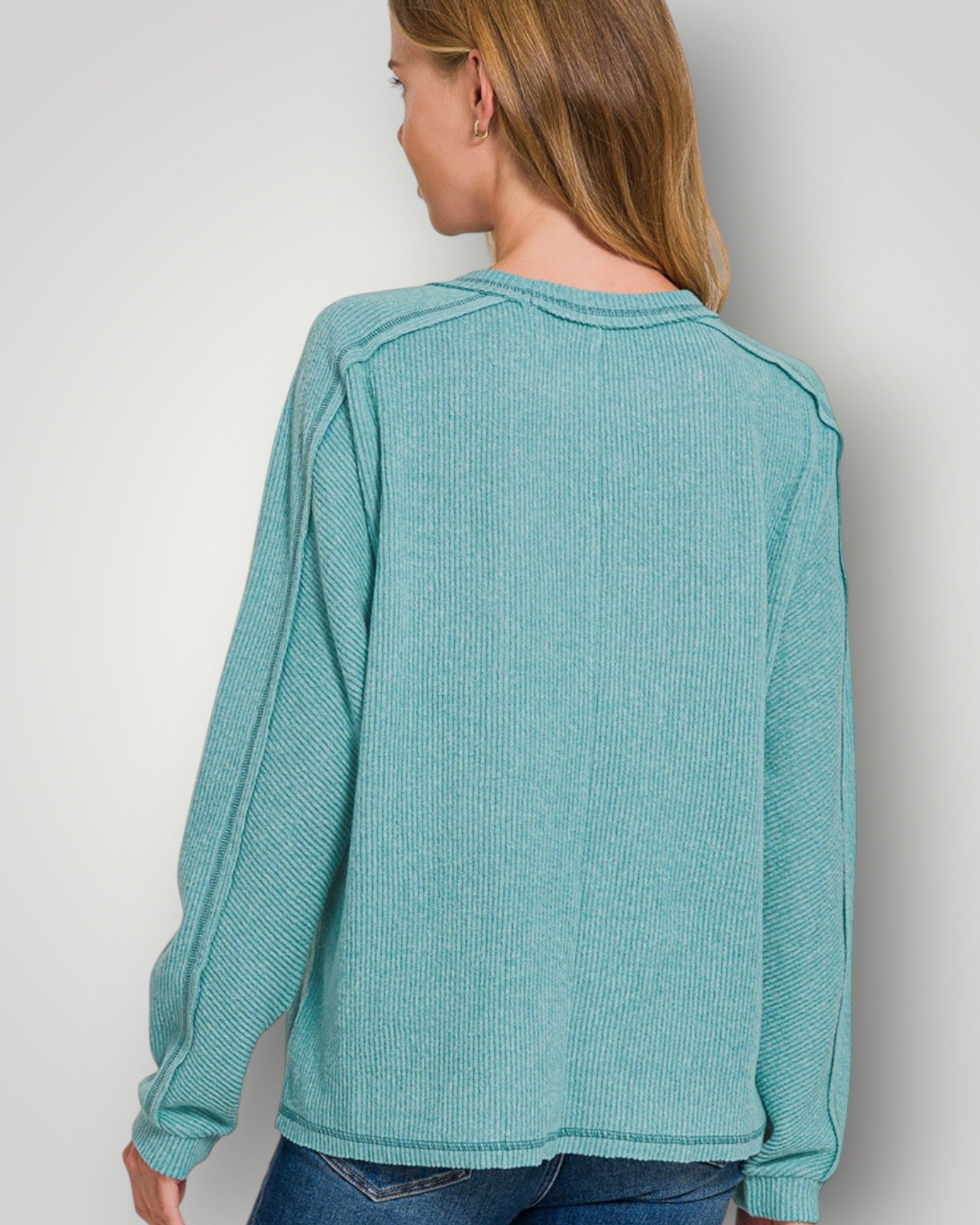 Person wearing a teal long-sleeve shirt against a plain background